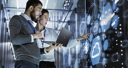 Two business professionals looking at digital displays showing cloud computing icons and data visualization in a modern office setting