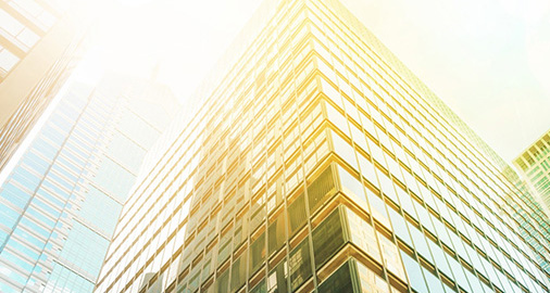 Modern glass office building photographed from below with sun reflection creating a golden glow effect